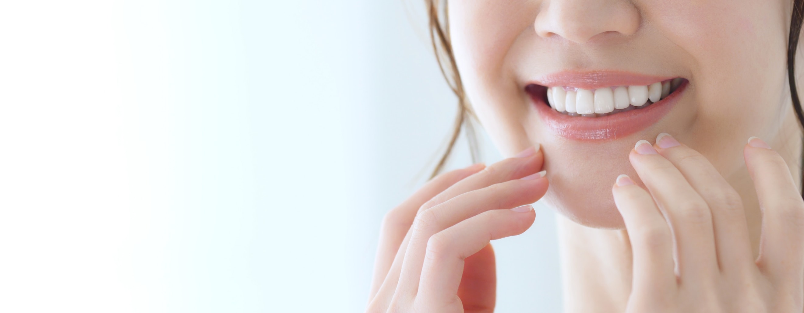 白く美しい歯を見せる笑顔の女性の口元と手元の写真